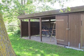 Ett takförsett utomhusområde med en träkonstruktion, en cykel och ett träd.