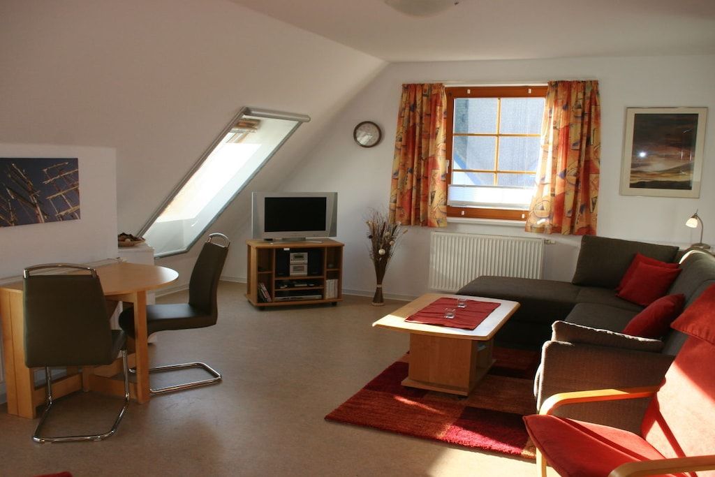 A living room with a television, a dining area with a table and chairs, a sofa, and a window with curtains.