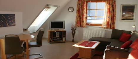 A living room with a television, a dining area with a table and chairs, a sofa, and a window with curtains.
