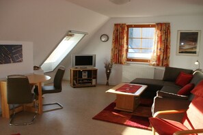 A living room with a television, a dining area with a table and chairs, a sofa, and a window with curtains. - Holiday home in Born with swimming pool (Born)