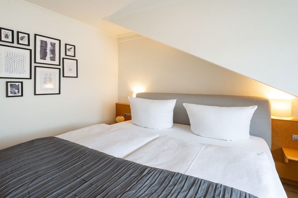 A hotel room with a bed, a headboard, a nightstand, and wall art.