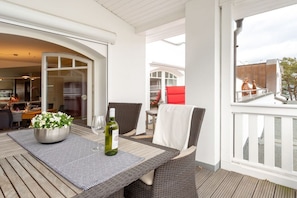 A covered outdoor dining area with a table, chairs, and a bottle of wine. - Penthouse Villa Gudrun with private sauna (Ostseebad Binz)