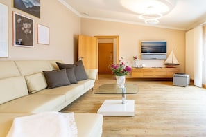 A modern living room with a sofa, a coffee table, a TV, and a wooden cabinet. - Penthouse Villa Gudrun with private sauna (Ostseebad Binz)