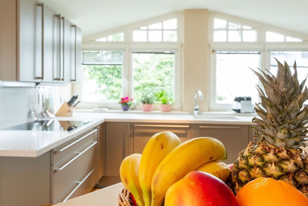 A kitchen with a fruit bowl containing bananas, a pineapple, and an orange.