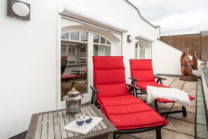 A rooftop terrace with red lounge chairs, a table with a lantern, and a statue. - Penthouse Villa Gudrun with private sauna (Ostseebad Binz)