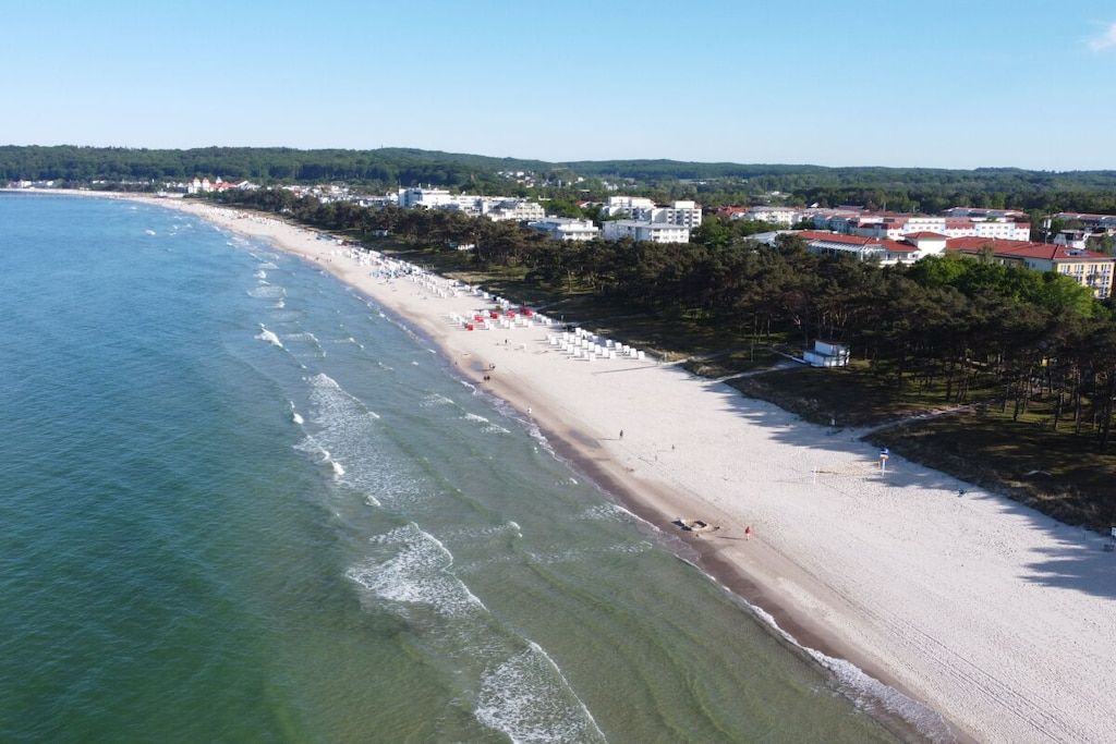 A coastal beach with a sandy shore, a clear blue sea, and buildings in the background.