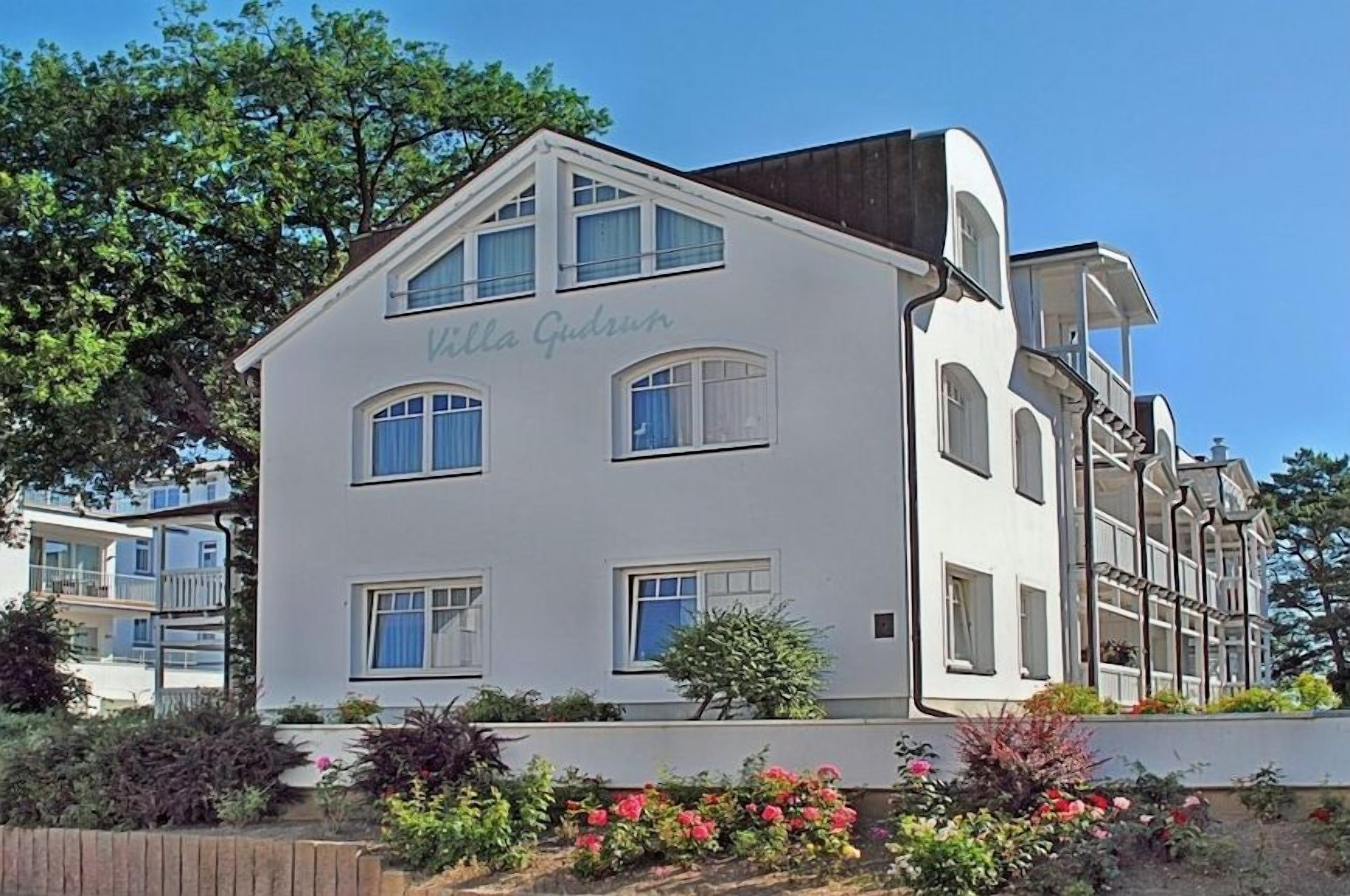 A white building with the name 'Villa Gudrun' on the facade, featuring multiple windows and balconies.