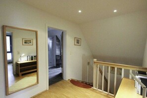 A room with a wooden floor, a mirror, a door leading to another room, and a staircase with a wooden railing. - Holiday home in Zingst with swimming pool (Zingst)