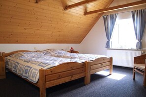 Ein Schlafzimmer mit einem hölzernen Bett, einem Fenster mit Vorhängen, einer Heizung und einem Sessel.