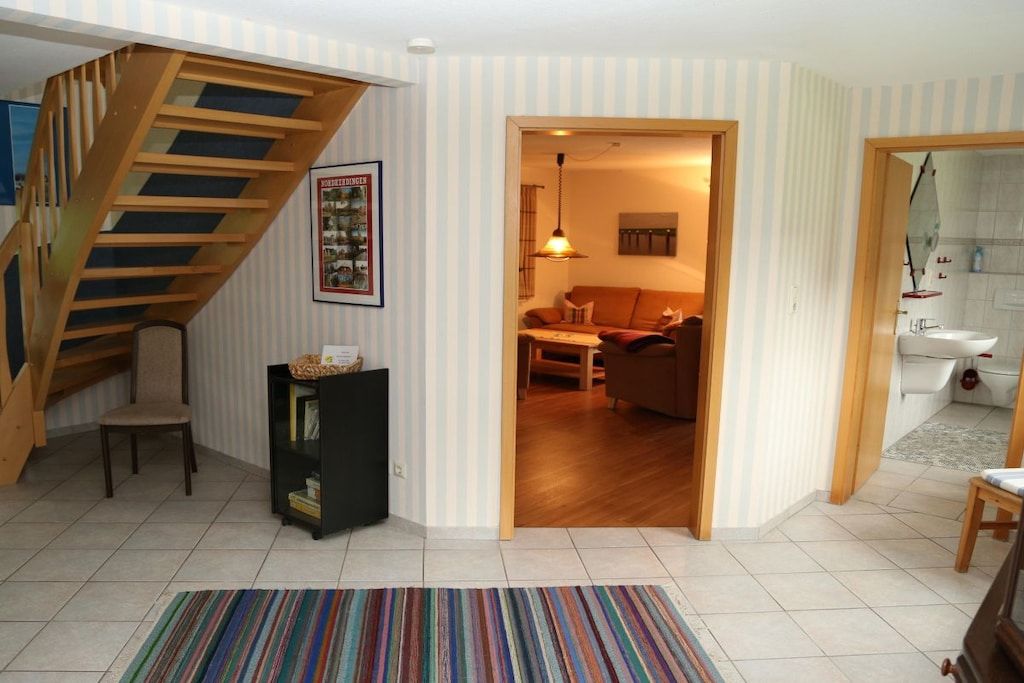 Eine Treppe führt zu einer oberen Etage, einem Wohnbereich mit Sofa und Tisch sowie einem Badezimmer mit Waschbecken und Spiegel.