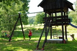 Eine Spielkonstruktion aus Holz mit Schaukel und Rutsche, umgeben von viel Grün.