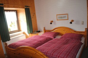 Ein Bett mit Holzkopfteil, zwei Kissen und einer roten karierten Tagesdecke.