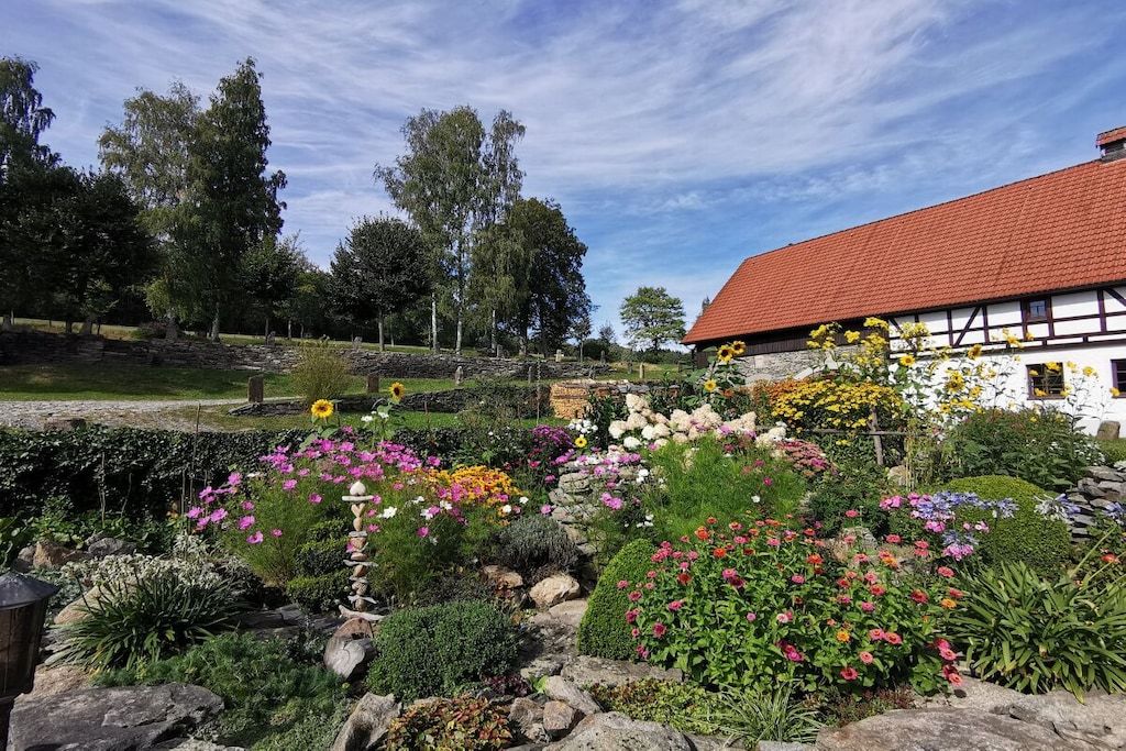 Een tuin met verschillende bloemen en een wit gebouw met een rood dak.