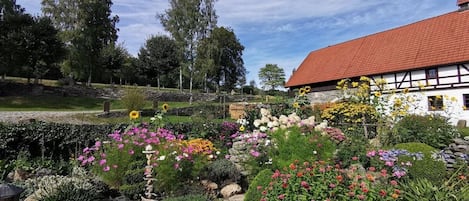 A garden with various flowers and a white building with a red roof.