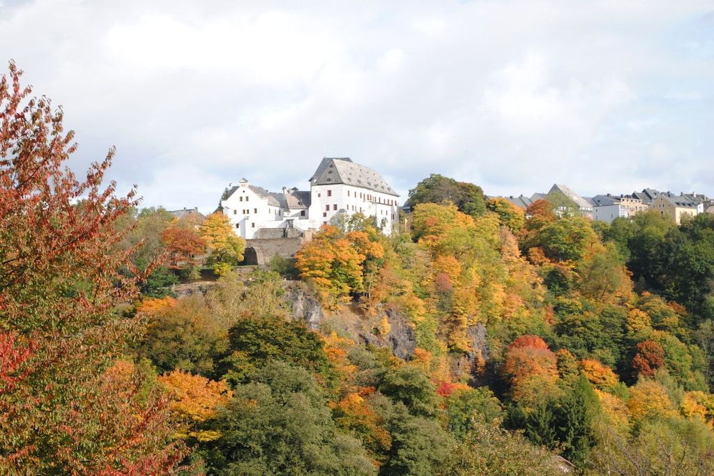 A large white building with multiple roofs, surrounded by autumn-colored trees.