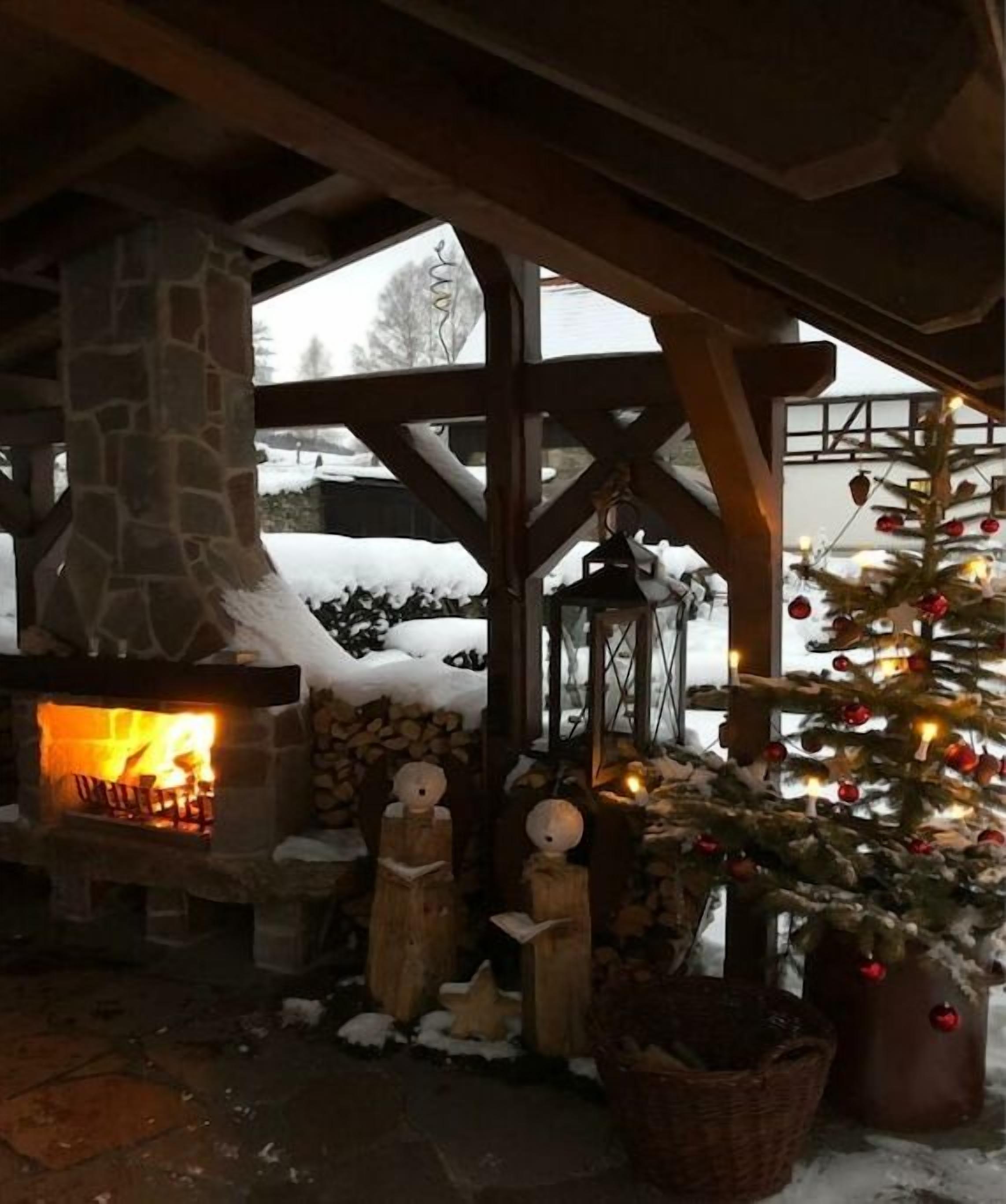 A stone fireplace with logs, a snow-covered roof, and a decorated Christmas tree.