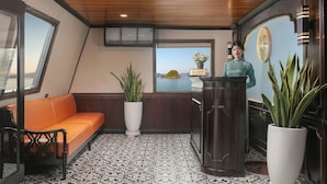 Een receptiezone met een houten plafond, een bank, een potplant, een receptiebalie en uitzicht op een waterpartij door een raam.