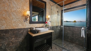 Een badkamer met een marmeren wand, een grote spiegel, een wastafel, een douche en uitzicht op zee.