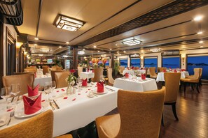 A dining area with tables set for two, featuring white tablecloths, red napkins, and glassware. - Halong Arcadia Cruise (Ha Long)