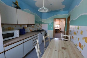 A kitchen with white cabinets, a microwave, a sink, and a wooden dining table. - Holiday apartment with 1 bedroom (Lübbenau)