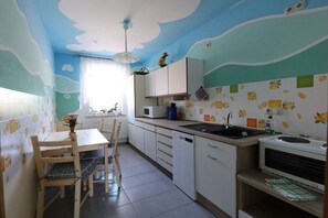 A kitchen with a white countertop, a sink, and cabinets. There is a dining table with chairs and a vase of flowers. - Holiday apartment with 1 bedroom (Lübbenau)
