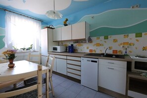 Une cuisine avec des meubles blancs, un lave-vaisselle et un four à micro-ondes. Il y a une fenêtre avec des rideaux et un vase de fleurs sur la table.
