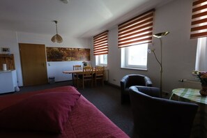 Une pièce comprenant un lit, un bureau, une chaise, une lampe et une fenêtre avec des stores.