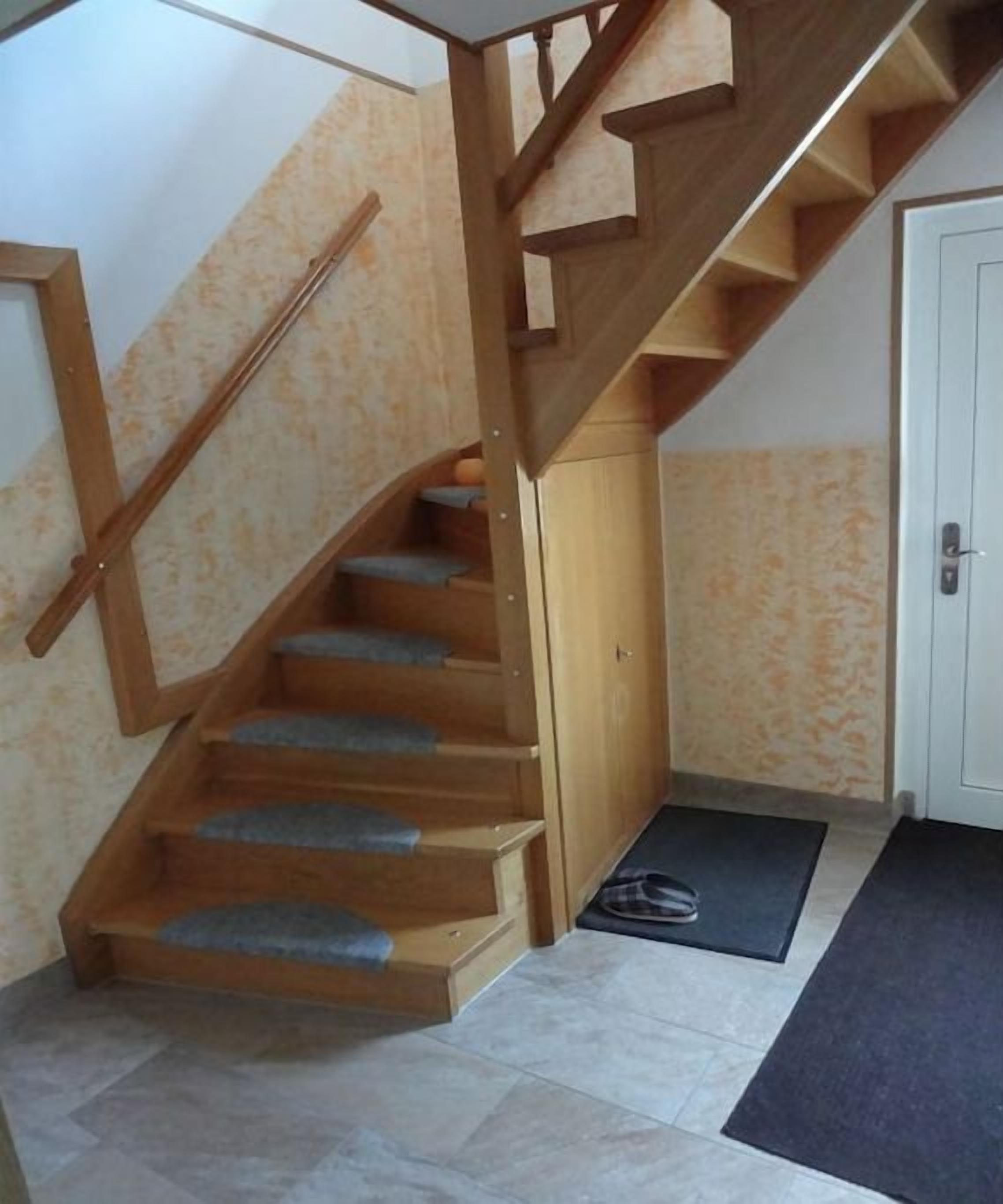 Una escalera de madera con barandilla, una puerta y un felpudo al final.