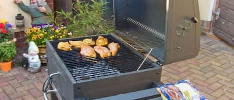 Un barbecue avec de la nourriture, une table avec des assiettes et une terrasse en briques.
