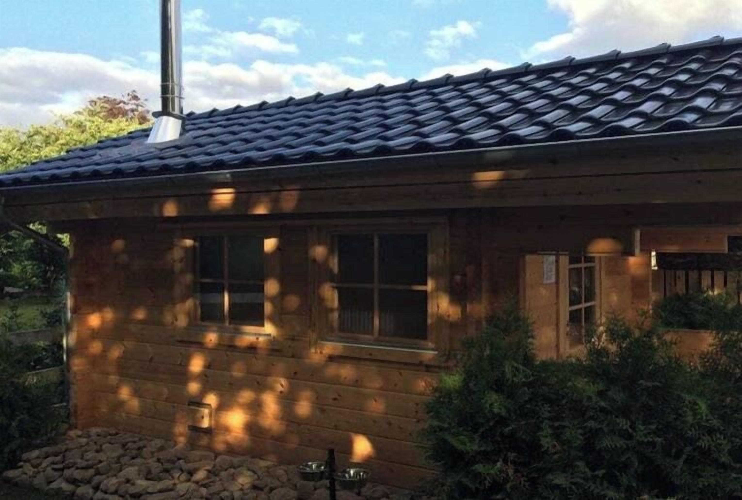 Une cabane en bois avec un toit en tuiles, des fenêtres et une cheminée.