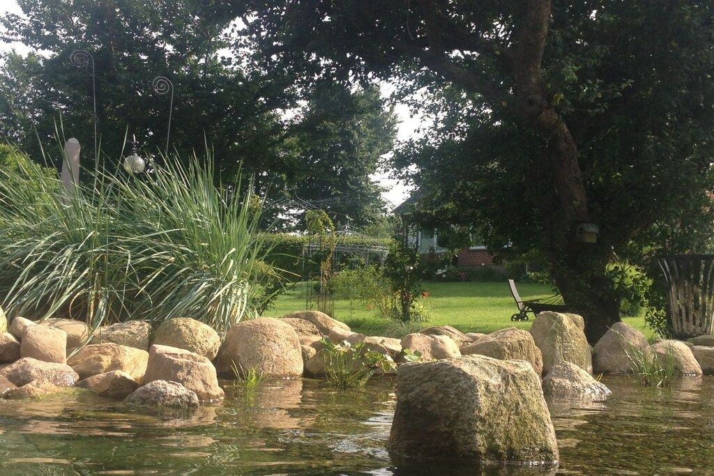 A tranquil garden with a pond, large rocks, and lush greenery.