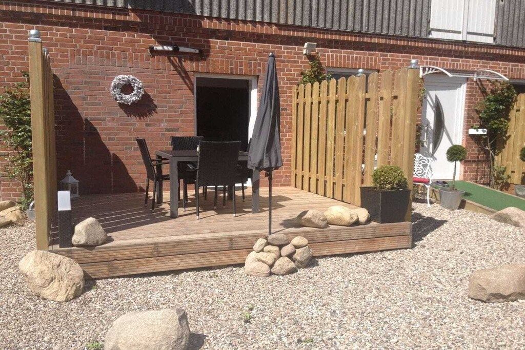 A patio with a wooden deck, outdoor furniture, and a gravel area with rocks.