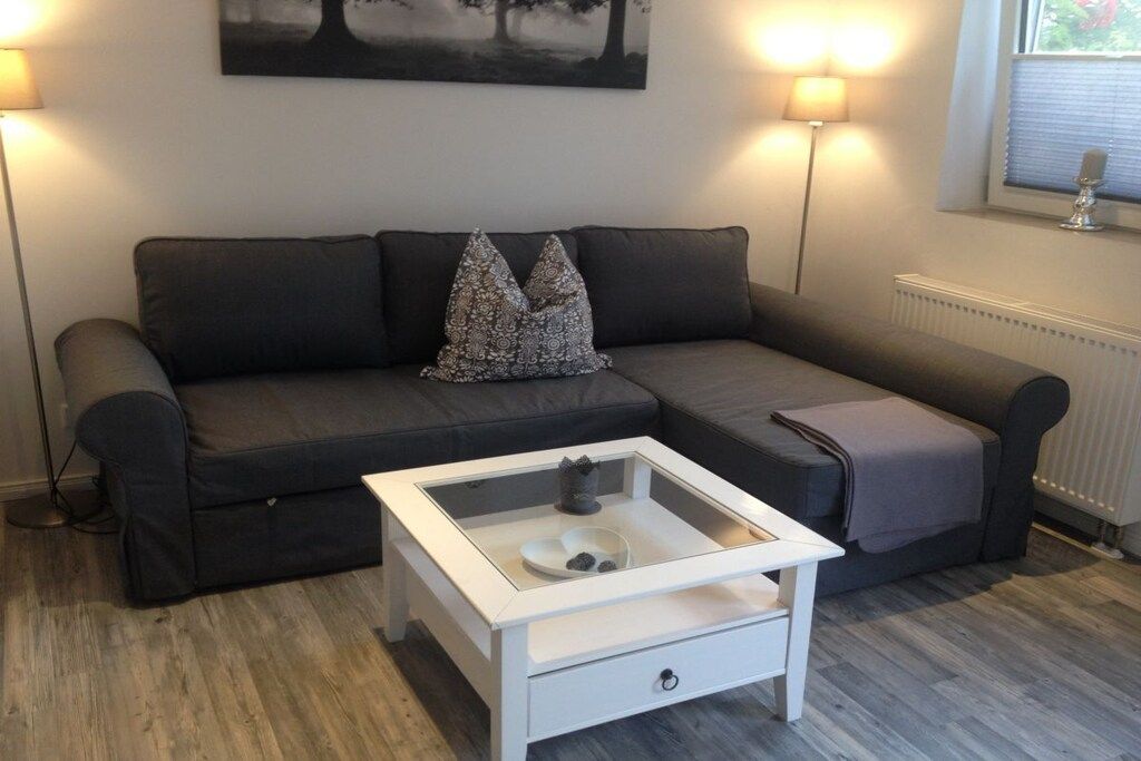 A modern living room with a grey sofa, a glass-top coffee table, and two wall-mounted lamps.