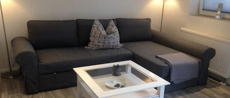 Un salon moderne avec un canapé gris, une table basse en verre et deux lampes fixées au mur.
