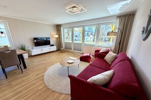 A modern living room with a sofa, a coffee table, a TV, and a dining area. - Holiday apartment KÜSTENNEST Baabe (Baabe)