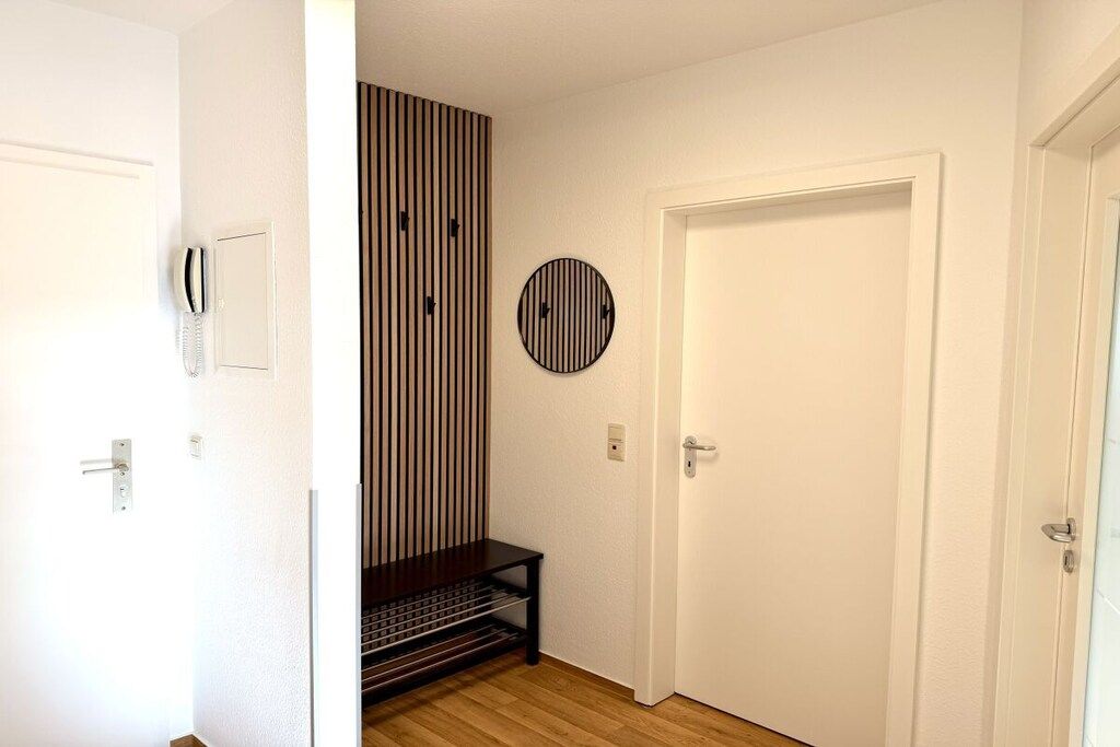 A hallway with a white door, a coat rack, a telephone, a striped wall panel, and a circular wall decoration.