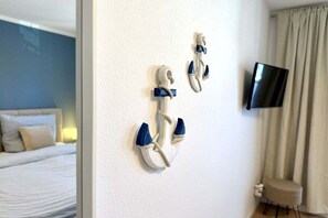 A room with a bed, a television mounted on the wall, and a decorative anchor on the wall. - Holiday apartment KÜSTENNEST Baabe (Baabe)