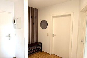 A hallway with a white door, a coat rack, a telephone, a striped wall panel, and a circular wall decoration. - Holiday apartment KÜSTENNEST Baabe (Baabe)