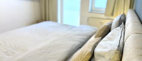 Un lit avec une tête de lit, un téléviseur fixé au mur et une fenêtre avec des rideaux.