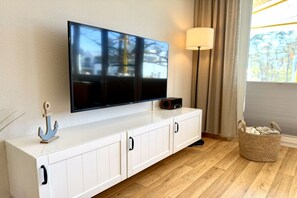 A flat-screen TV mounted on a white cabinet with a decorative anchor, a lamp, and a basket on the floor. - Holiday apartment KÜSTENNEST Baabe (Baabe)