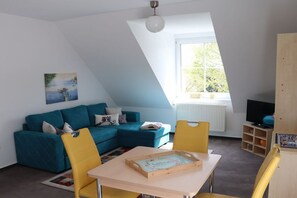 A modern living room with a blue sectional sofa, a yellow chair, a wooden table, and a painting on the wall. - Holiday apartment in Süsel with swimming pool (Süsel)