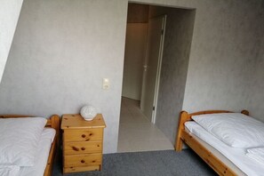 A bedroom with two wooden beds, a nightstand with a lamp, and a door leading to another room. - Holiday apartment in Süsel with swimming pool (Süsel)