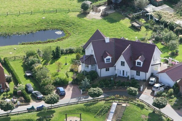 A large white house with a red-tiled roof, surrounded by a well-maintained lawn and a small pond. - Holiday apartment in Süsel with swimming pool (Süsel)