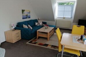 A cozy living room with a blue sofa, a wooden coffee table, a yellow chair, and a small table with a box. - Holiday apartment in Süsel with swimming pool (Süsel)