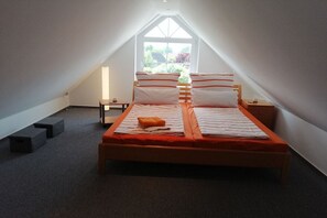 A bedroom with a sloped ceiling, a bed with striped bedding, a small bedside table, and a window with a view of greenery. - Holiday apartment in Süsel with swimming pool (Süsel)