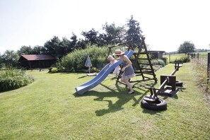Une aire de jeux avec un toboggan et des structures d’escalade, située dans un espace herbeux.