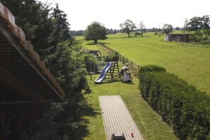 Ein Spielplatz mit einer Rutsche und einem kleinen Spielhäuschen in einer grünen Wiese.