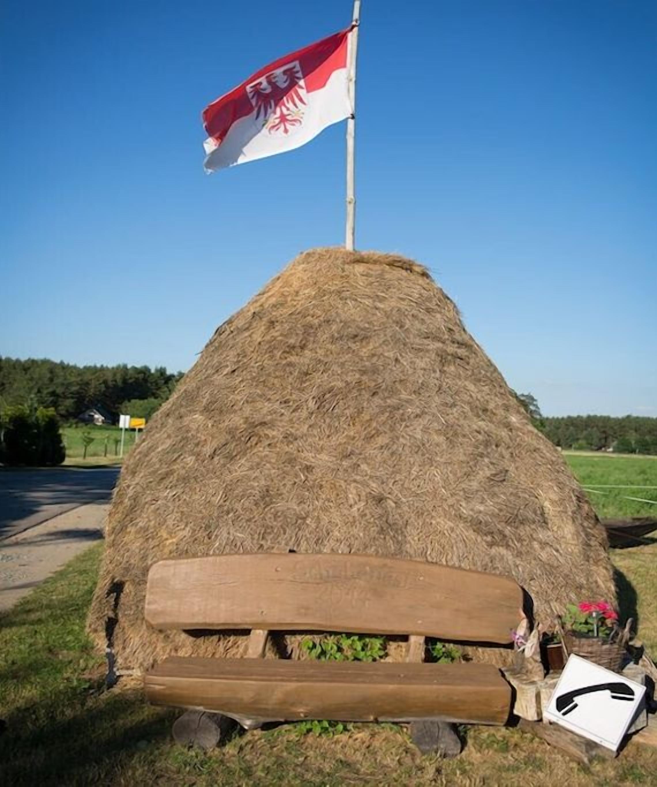 A hay bale with a flag on top, a wooden bench, and a small table with a flower.