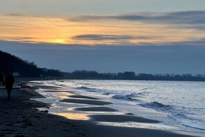 Ein Strand mit ruhiger See, einigen Spaziergängern und einem Sonnenuntergang im Hintergrund.