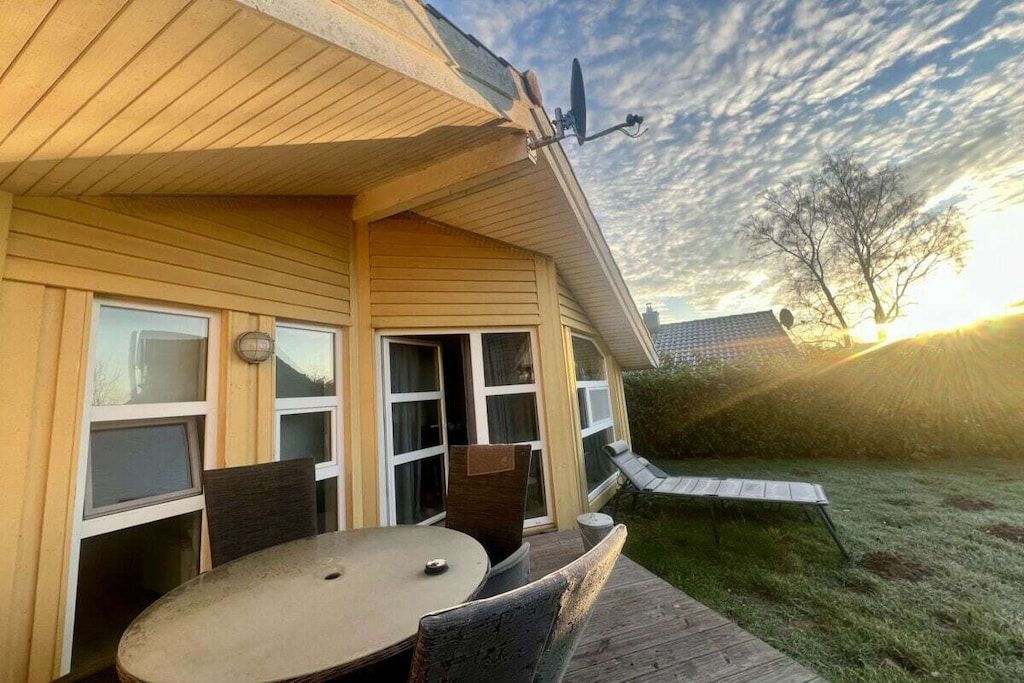 Una terraza de madera con una mesa y sillas, un porche cubierto y una antena parabólica.